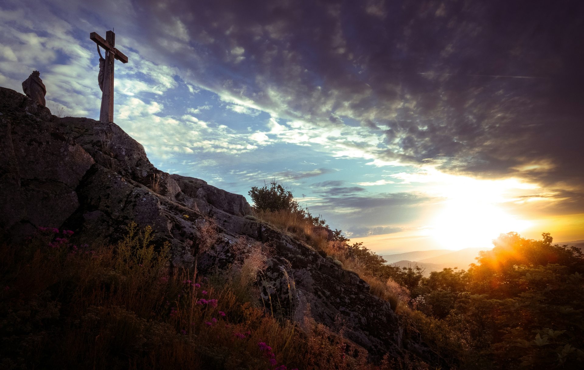 A wooden cross on a hill at sunset